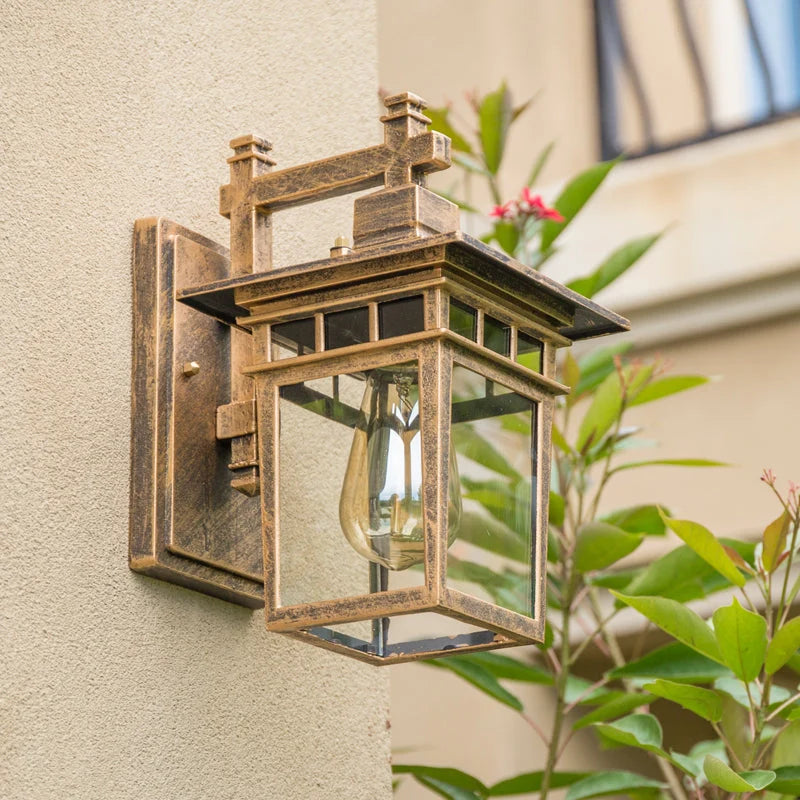 Clear Glass Outdoor Wall Lantern - Antique Bronze Finish Beside Plants