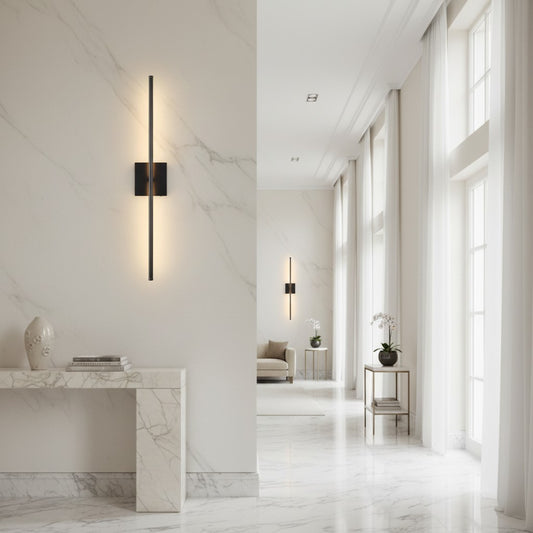 Lorvali modern black iron linear LED wall sconce mounted on a white marble wall in a bright, minimalist hallway.
