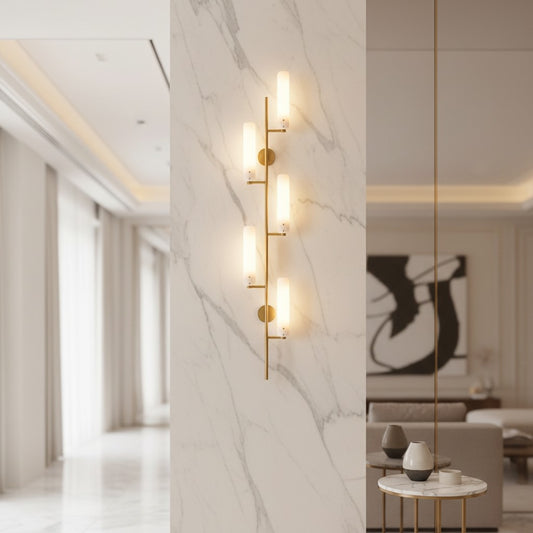 Lorvali four-head wall light with brass finish and cylindrical glass shades mounted on a white marble pillar
