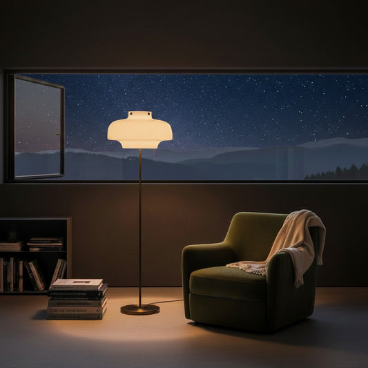 Lorvali Copenhagen floor lamp with opal glass shade and antique bronze stem beside a green armchair at night.