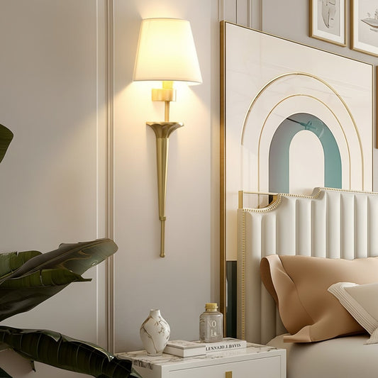 Lorvali modern gold copper wall sconce with white fabric shade mounted in a stylish bedroom interior