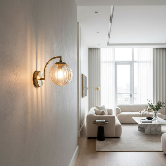 Lorvali modern gold wall sconce with a clear ribbed glass ball shade mounted on a white wall in a living room