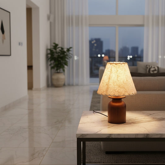 Lorvali Koru table lamp with a walnut rubber wood base and textured parchment shade glowing on a marble side table