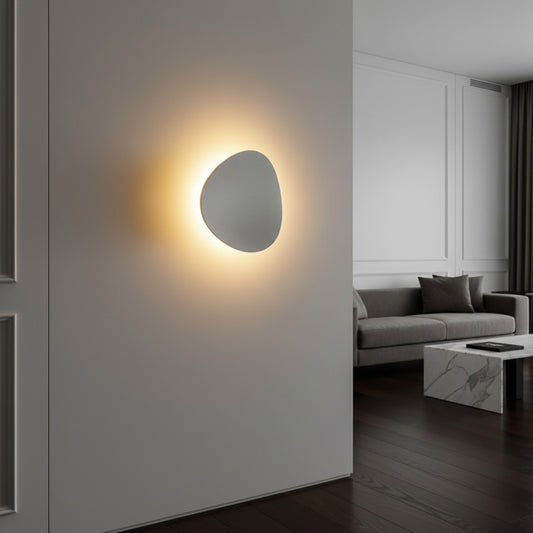 Lorvali minimalist white LED wall sconce with a pebble-shaped design casting a warm glow on a modern living room wall.