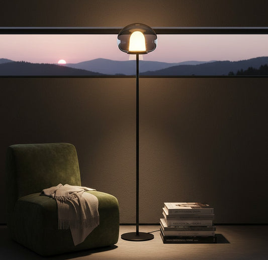 Lorvali Thea floor lamp with a smoke gray glass globe and warm LED light next to a green armchair at sunset